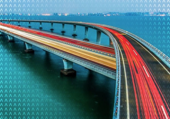Image of a long-spanning bridge over a body of blue water with abstract color flashes implying speeding information/data.