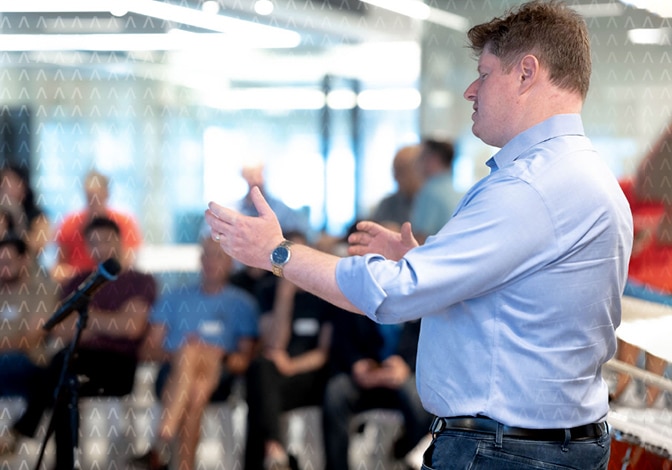 Lior Yogev stands in front of the global FundGuard team. Viewed from the side, he is wearing a blue shirt and dark jeans.